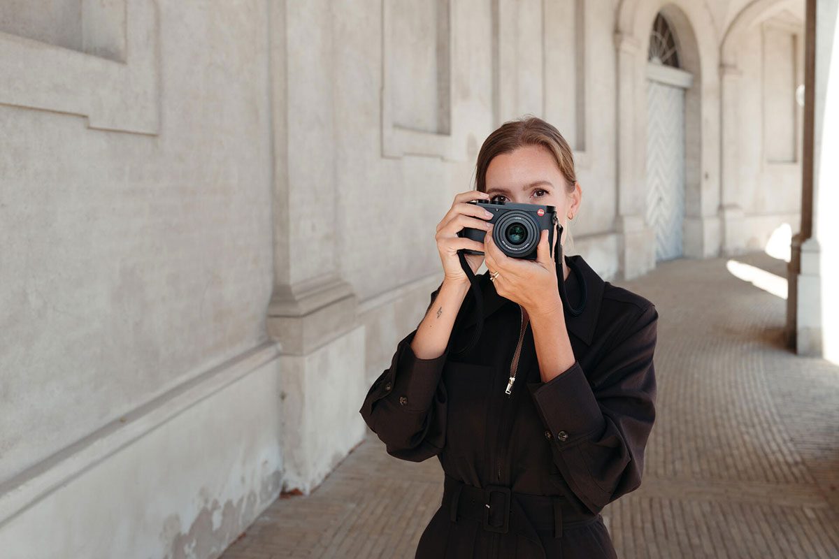 Eine Frau hält eine Fotokamera in den Händen und blickt direkt in die Kamera