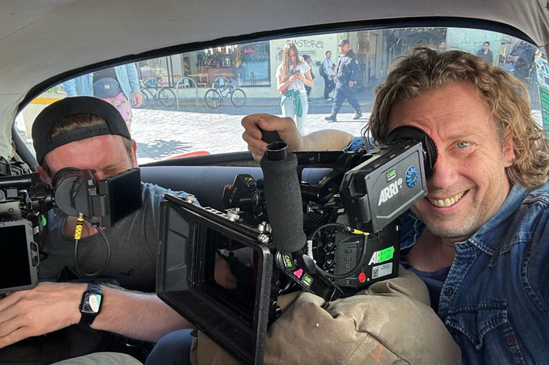 Maher Maleh sitzt in einem Auto und schaut durch eine professionelle Filmkamera