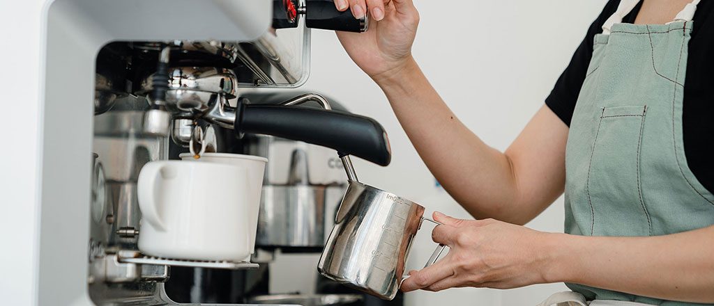 TF_esprotec_Visual Eine Frau schäumt Milch an einer professionellen Kaffeemaschine auf