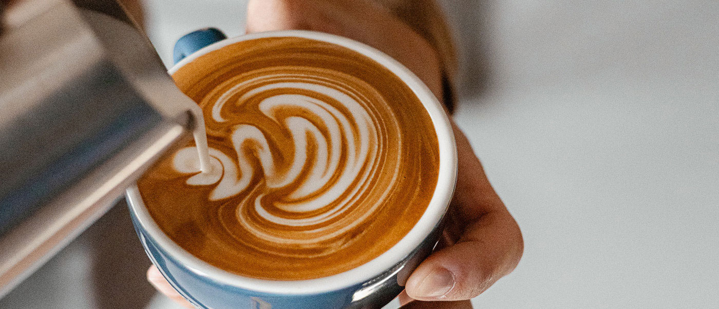 espressonisten-01 Ein Barista gießt Milch in eine Kaffeetasse und malt damit ein Muster